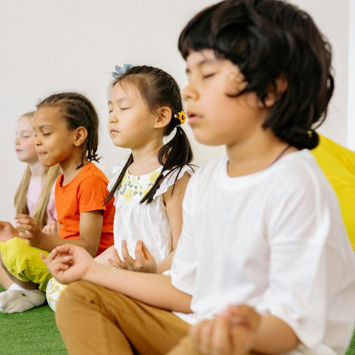 Kinderen zitten met gesloten ogen op de grond tijdens een mindfulnessles